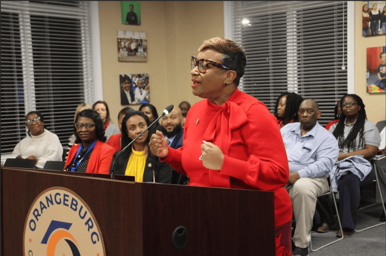 Educator speaking at recognition event in front of engaged audience.
