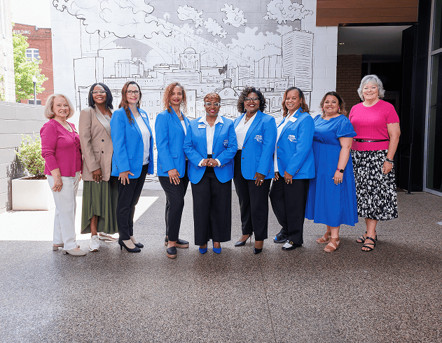 Diverse team of women professionals at EPI Center in front of city mural.